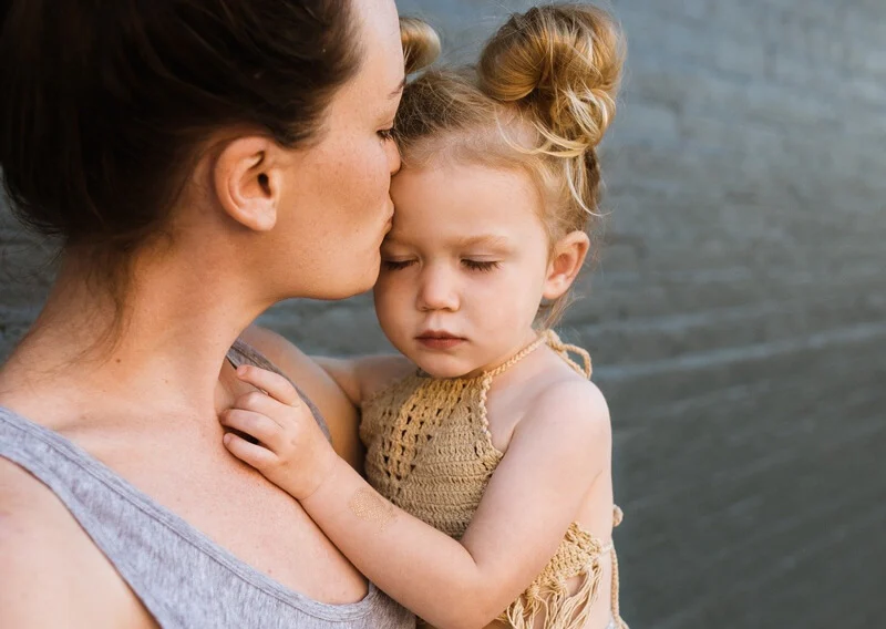 Donna che ha in braccio una bambina a cui dà un bacio