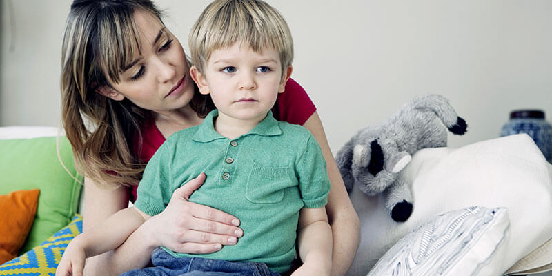 Mamma con un bambino in braccio che gli tocca la pancia, seduti su un divano